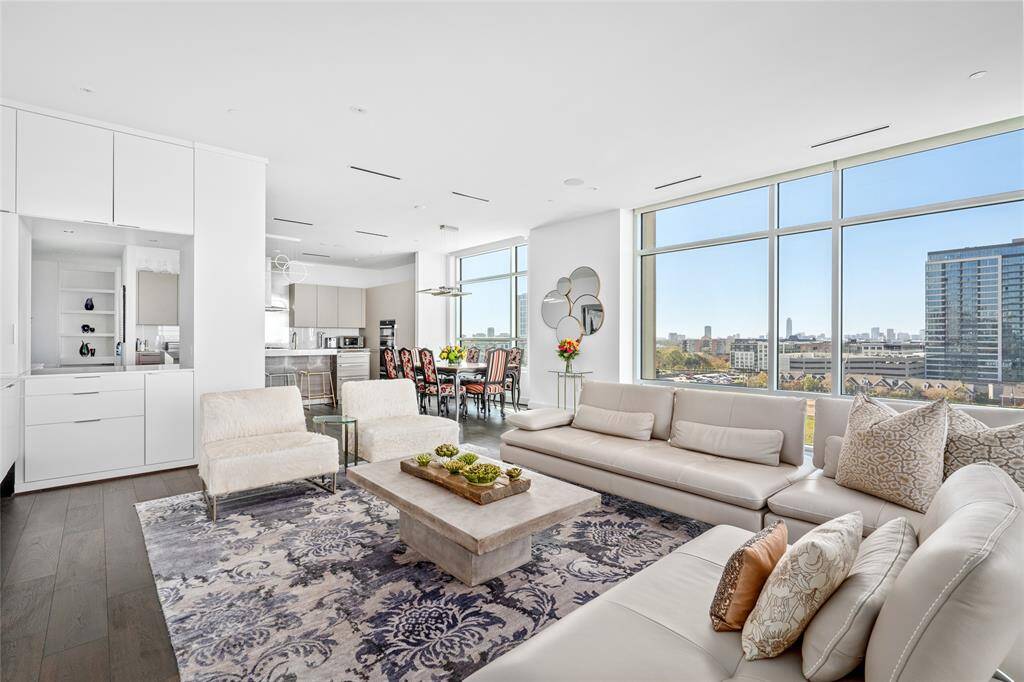 Beautifully illuminated by expansive windows and stunning views, the open concept creates a seamless flow from the living area into the dining and kitchen spaces. The rooms are equipped with modern conveniences that enhance the comfort and entertainment, including automatic blinds and a Savant surround sound system. On the left, a sleek and functional dry bar area enhances the convenience and style of the layout.