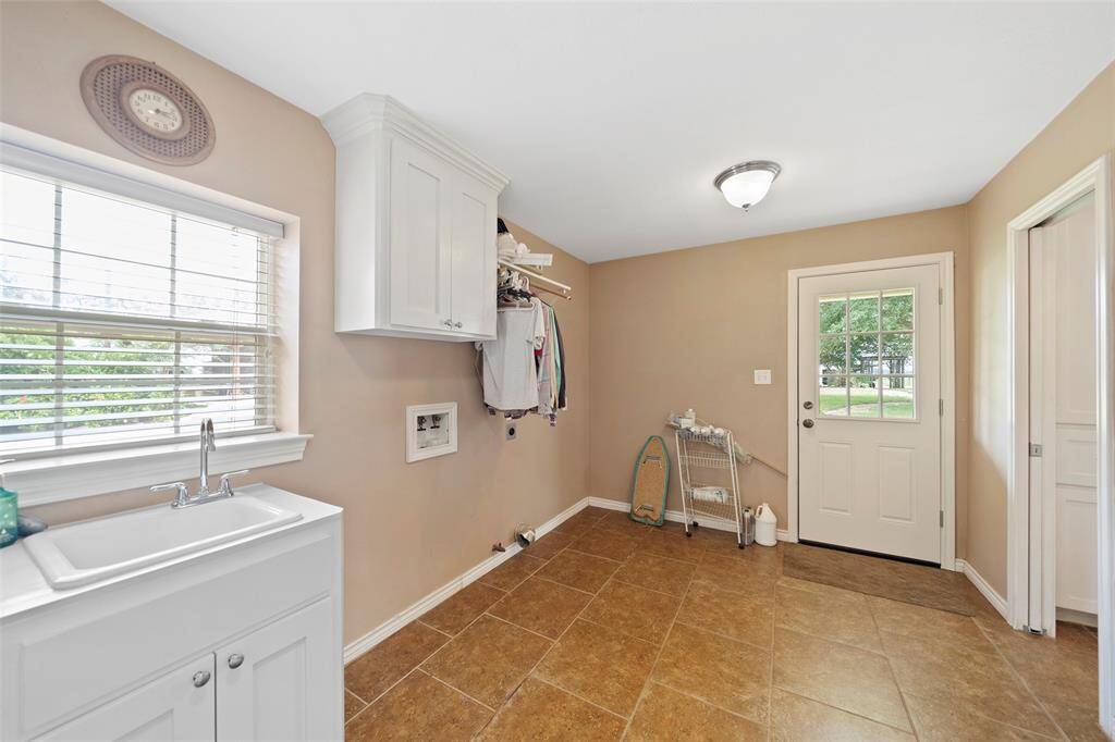 Oversized utility room with storage, hanging space, sink, and backyard access—ideal for everyday chores or muddy boots after barn time.
