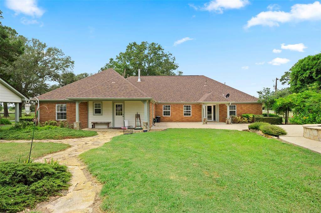 Spacious backyard with covered patio, open lawn, and mature trees—plenty of room to relax or play, just steps from the pool and outdoor kitchen.