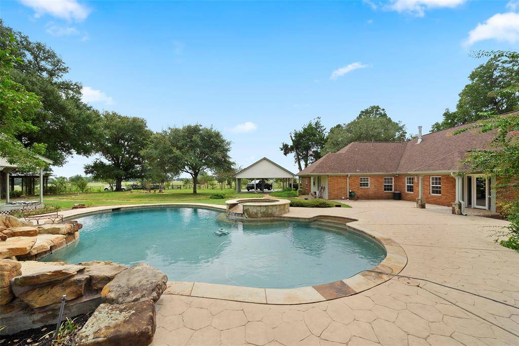 Resort-style pool and spa with natural stone accents and a wide deck for sunbathing, all set against peaceful country views.