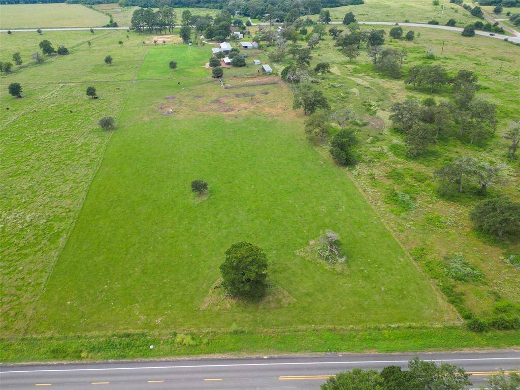 Drone view highlights the road frontage and depth of the property. Multiple access points and fence lines give structure while preserving the wide-open feel.