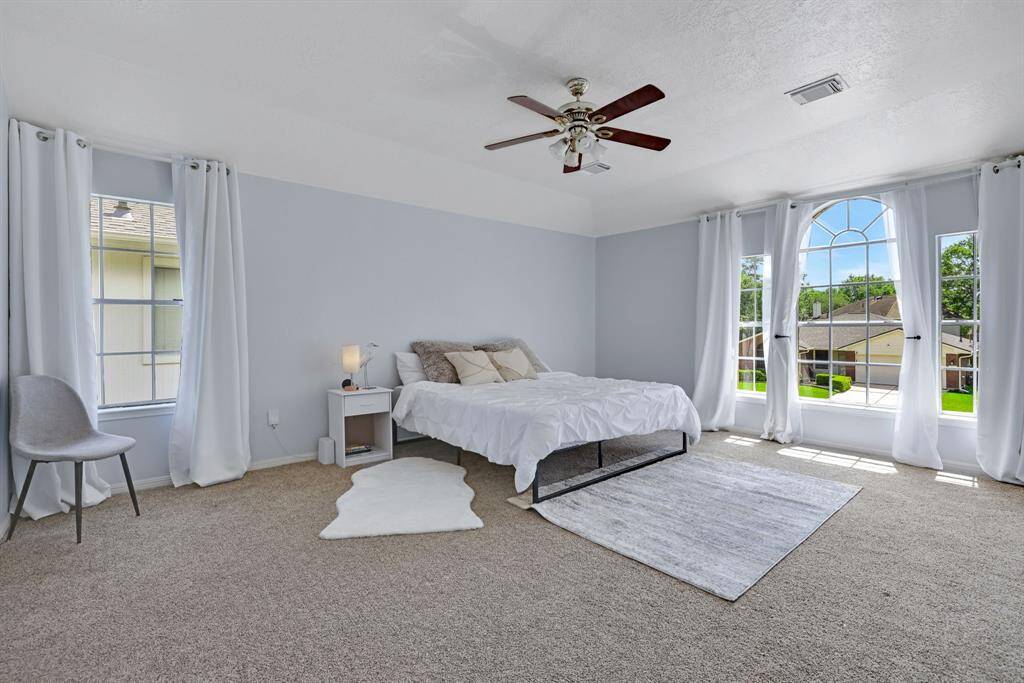 This spacious bedroom features large windows with plenty of natural light, neutral carpeting, and a ceiling fan.