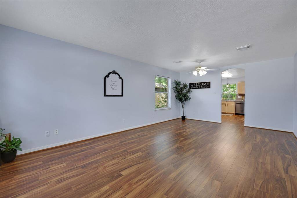 This spacious living area features elegant vinyl plank wood flooring look, ample natural light from a large window, and a seamless flow into the kitchen, perfect for entertaining and family gatherings.