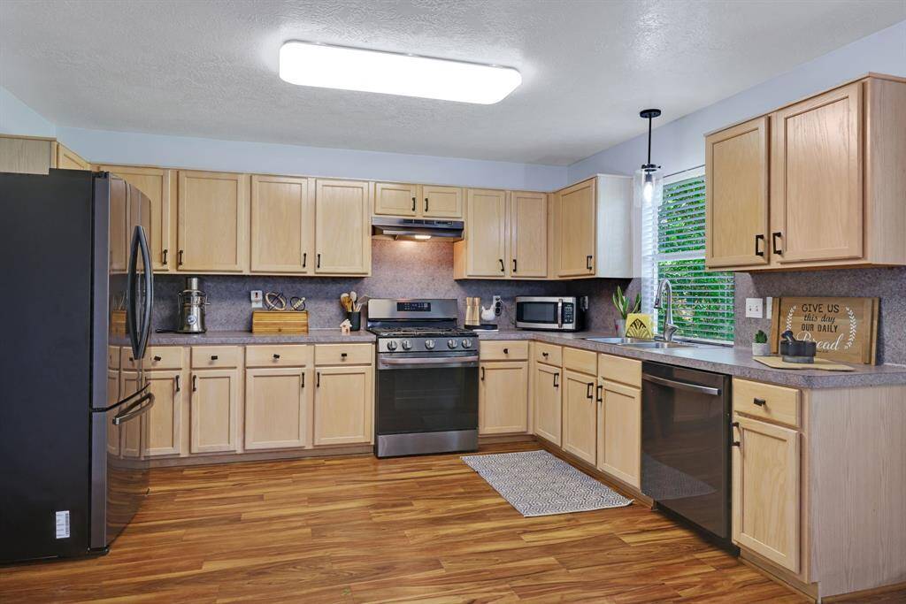 The kitchen features modern appliances, abundant light wood cabinetry, and warm vinyl plank flooring, creating a spacious and inviting cooking area.