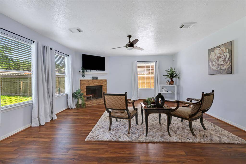 This spacious family room features hardwood floors, a cozy fireplace, and ample natural light from large windows offering a comfortable and inviting atmosphere.