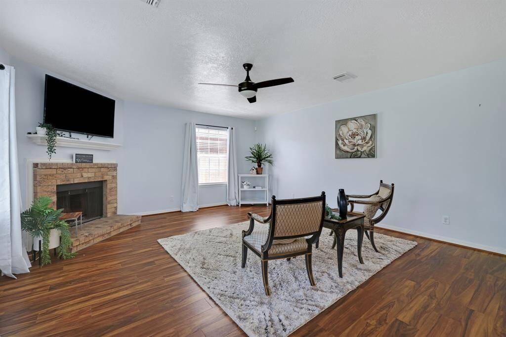 This inviting family room features vinyl plank floors and an open layout leading to a modern kitchen. Natural light flows through large windows, enhancing the airy feel.