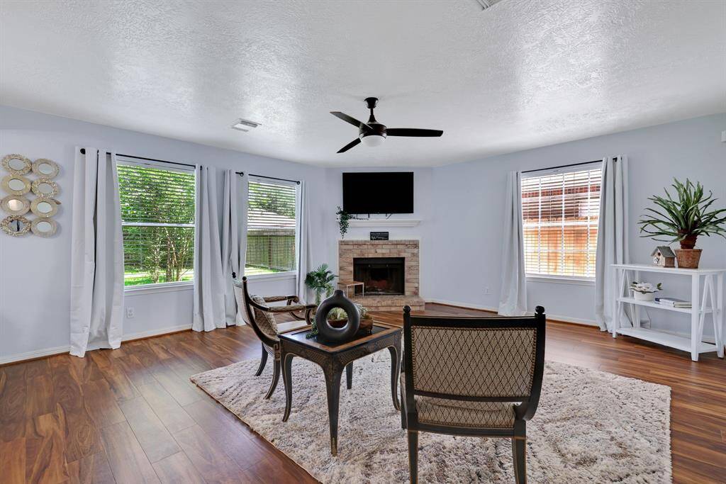 Bright and airy living room with large windows, hardwood floors, and a cozy fireplace. Features a ceiling fan, modern decor, and ample natural light, creating a welcoming atmosphere.