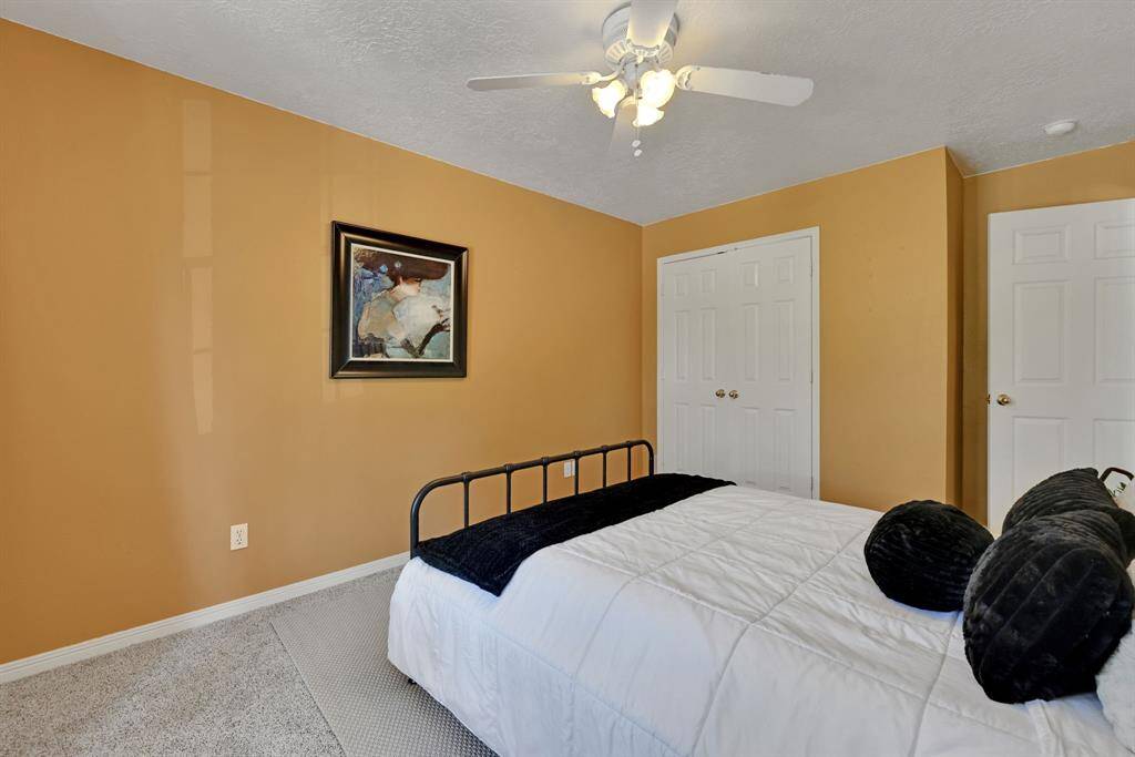 Cozy bedroom with warm-toned walls, featuring a ceiling fan, The room has a soft carpet and a closet with double doors, offering ample storage.