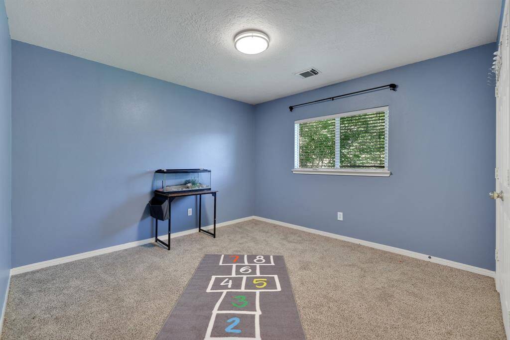 This room features soft blue walls and carpeted flooring, creating a cozy atmosphere. It includes a window with blinds for natural light and a ceiling light fixture.