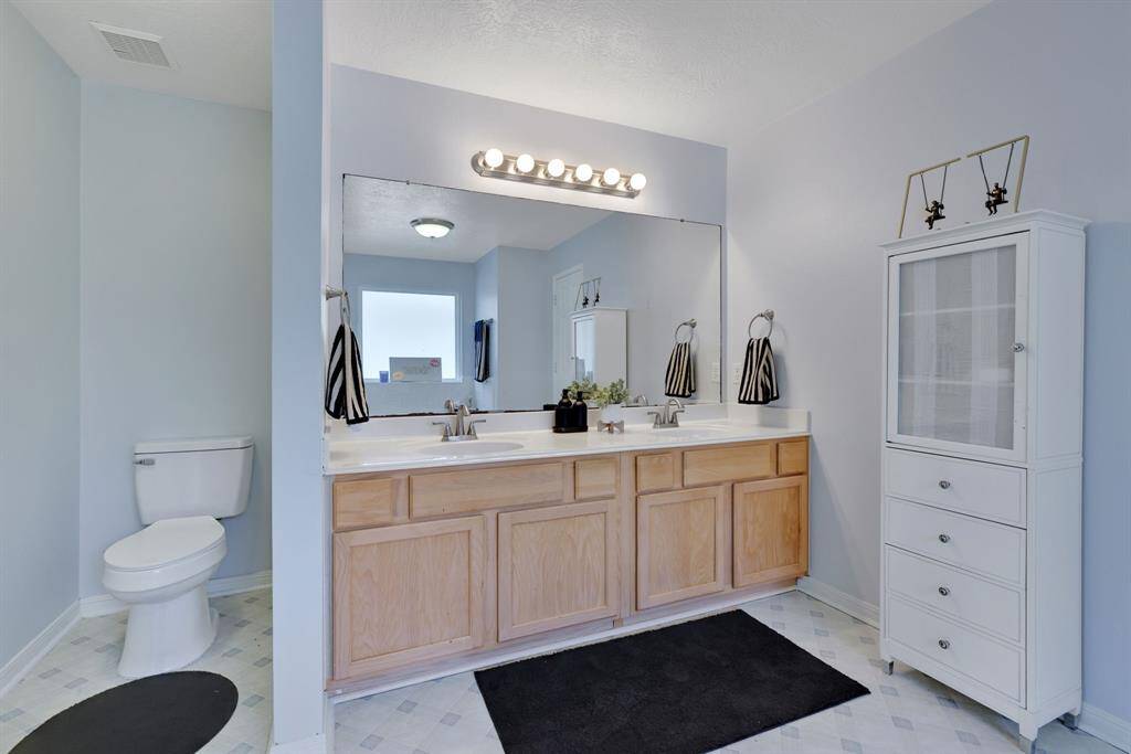This Primary bathroom features a spacious double vanity with ample storage, a large mirror, and modern lighting. It includes a toilet, sleek light-flooring.  The space is bright and functional.