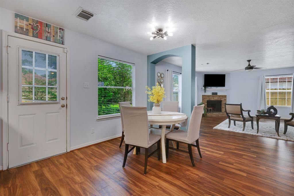 This inviting  breakfast area features warm vinyl plank flooring, and a bright living room with a fireplace. Large windows offer abundant natural light, and modern lighting fixtures enhance the contemporary feel.