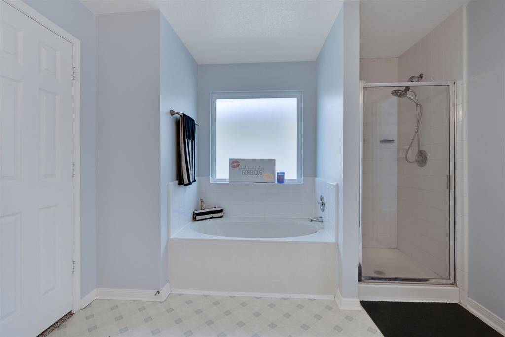 This en-suite  bathroom features a clean, modern design includes a spacious tub beneath a frosted window for natural light and privacy, alongside a separate glass-enclosed shower. The layout is practical and inviting, perfect for relaxation.