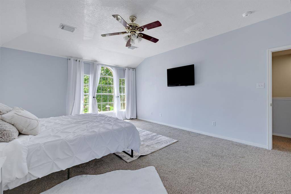 This spacious bedroom features large windows with plenty of natural light, neutral carpeting, and a ceiling fan.