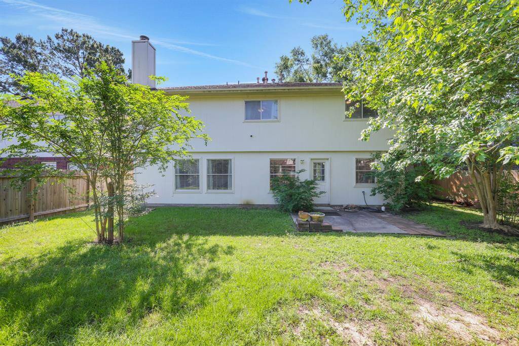 This backyard offers a spacious, grassy area with mature trees and a patio, perfect for outdoor activities and relaxation. The house features a two-story layout with large windows, enhancing natural light and garden views.