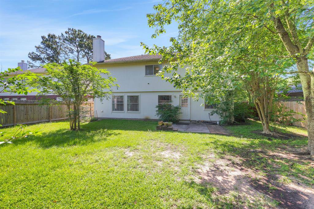 Spacious backyard with lush greenery, mature trees, and a patio area, perfect for outdoor activities and relaxation. The home's exterior features a two-story design with large windows and a fenced perimeter for privacy.