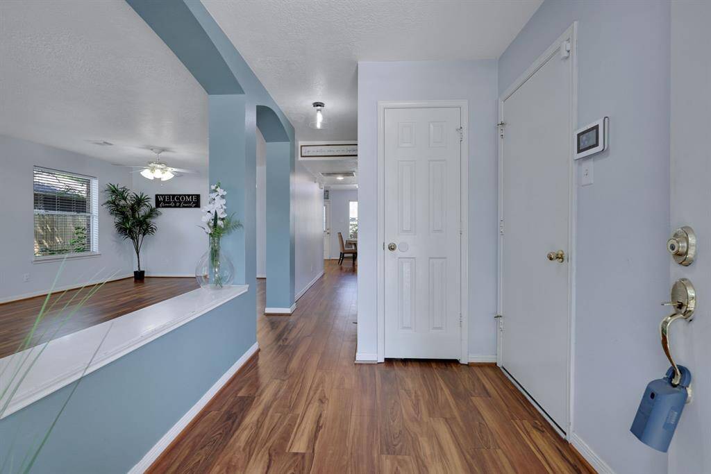 This welcoming entryway features a bright, open layout with light blue accent walls and warm wood look vinyl plank flooring. It leads into a spacious living area on the left, highlighted by large windows, a ceiling fan, creating an inviting atmosphere.