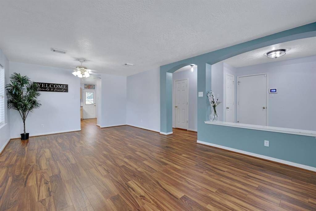 Bright and spacious living area with wood look flooring, light accent walls, and modern lighting. Features an open layout with a welcoming atmosphere, perfect for family gatherings.