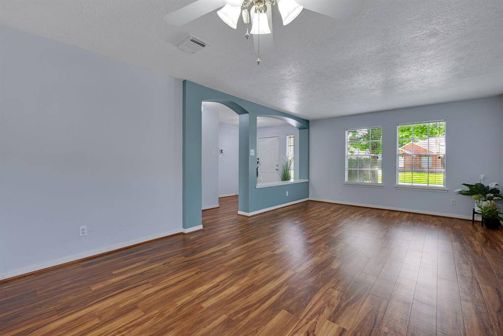 Bright and spacious living area with wood look flooring, light accent walls, and modern lighting. Features an open layout with a welcoming atmosphere, perfect for family gatherings.
