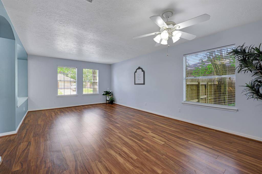 This spacious living room features elegant hardwood flooring, abundant natural light from large windows, and a ceiling fan. It's a perfect, airy space for relaxation or entertaining.