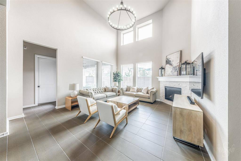 Dramatic two-story family room featuring a wall of windows, a cozy fireplace, lovely tile flooring and neutral tones throughout. A perfect space for relaxing with family or hosting friends.