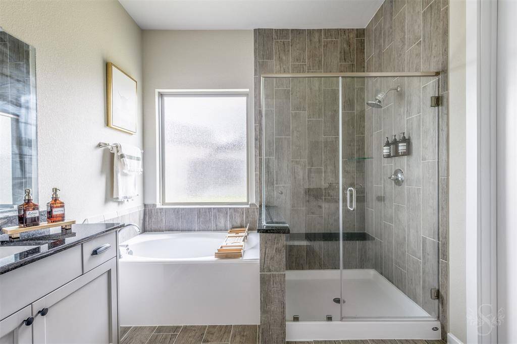 The luxurious primary bath features a walk-in enclosed shower with tile surround, a soaking tub, and granite-topped vanities. A private retreat for daily relaxation.