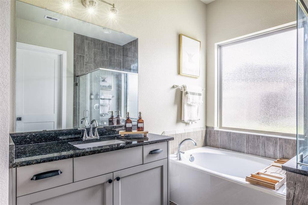 Light and bright primary bathroom with a soaking tub under an opaque window, granite vanity counters, and plenty of storage. The ideal blend of function and comfort.