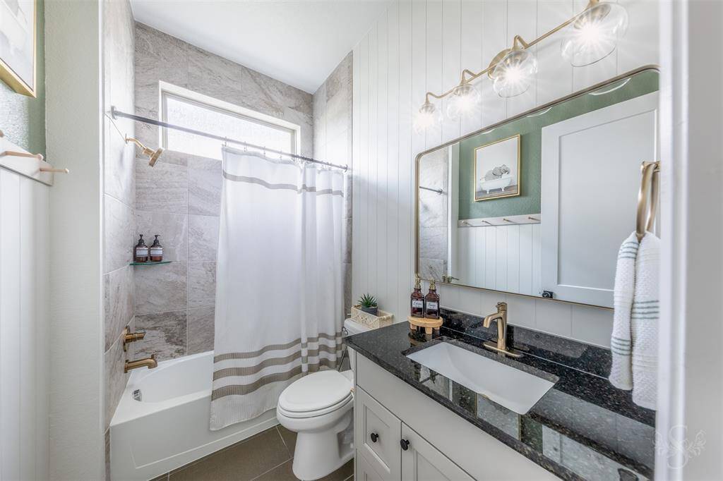 En-suite to the secondary bedroom on the 1st floor, this modern bath features shiplap accent walls, granite counters, updated fixtures and hardware, and a tiled shower/tub combination offering both style and functionality.