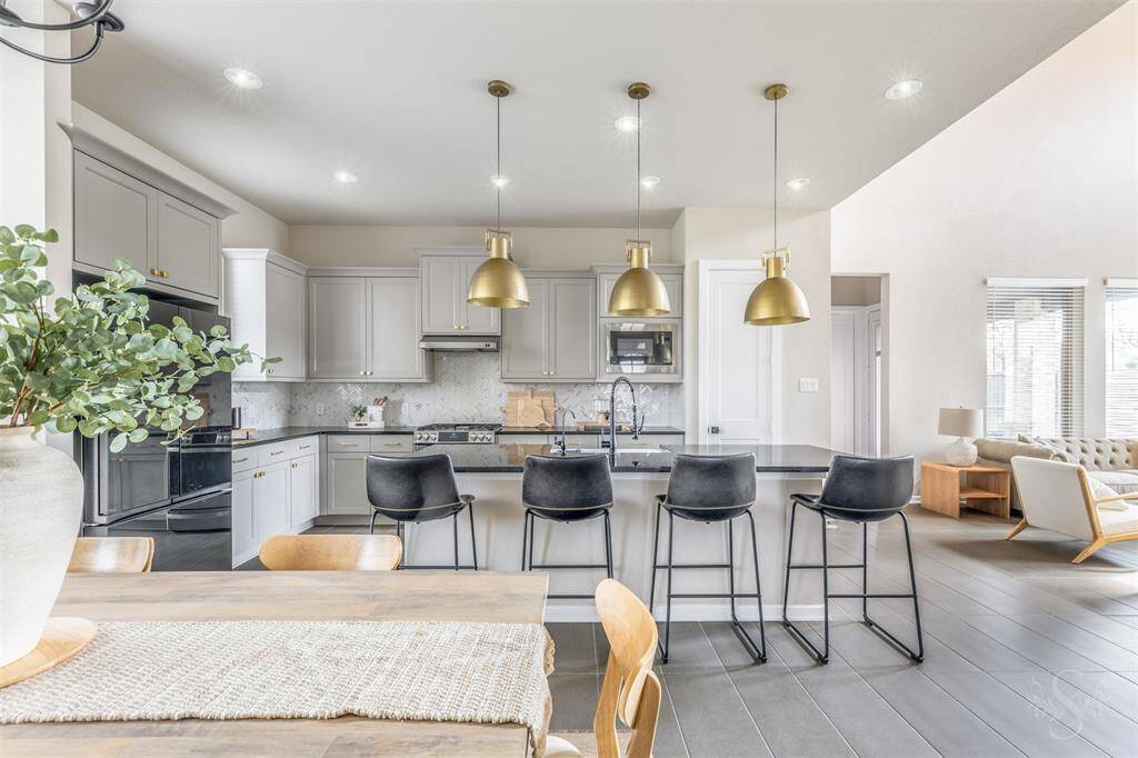 The chef’s kitchen boasts popular gray cabinetry with upgraded handles and knobs, undercabinet lighting, stainless steel appliances, farmhouse sink, a herringbone backsplash, and a granite island with breakfast bar. Elegant gold pendant lighting adds a luxurious touch to this beautiful gathering space.