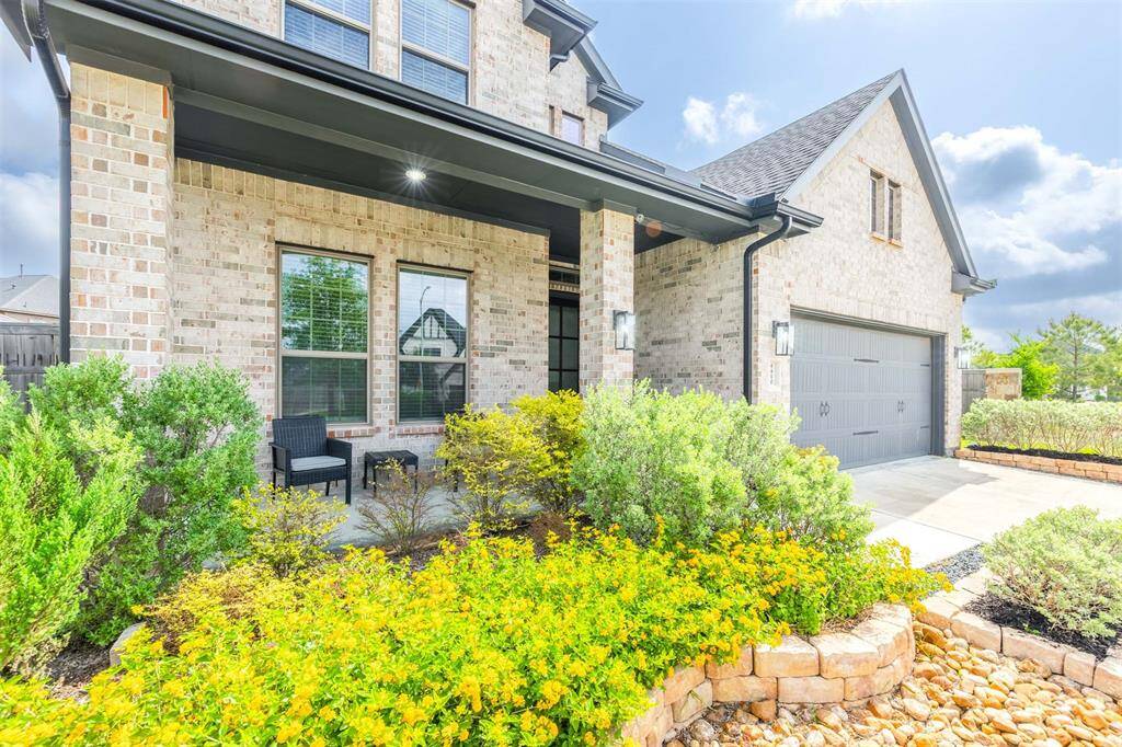 Charming front porch with seating area surrounded by upgrade lush landscaping and vibrant flower beds. A welcoming brick exterior and elegant elevation create fantastic curb appeal.