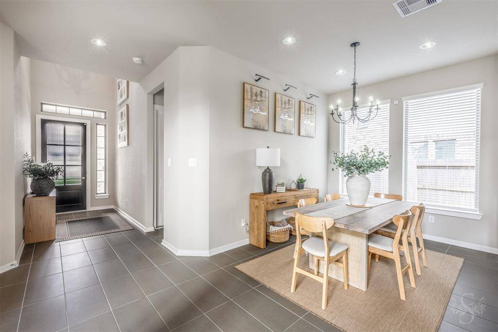 Bright and inviting dining area just off the entry, featuring large windows, recessed and new chandelier lighting, and stylish tile flooring. Perfect for gathering with family and friends in an open, airy setting.