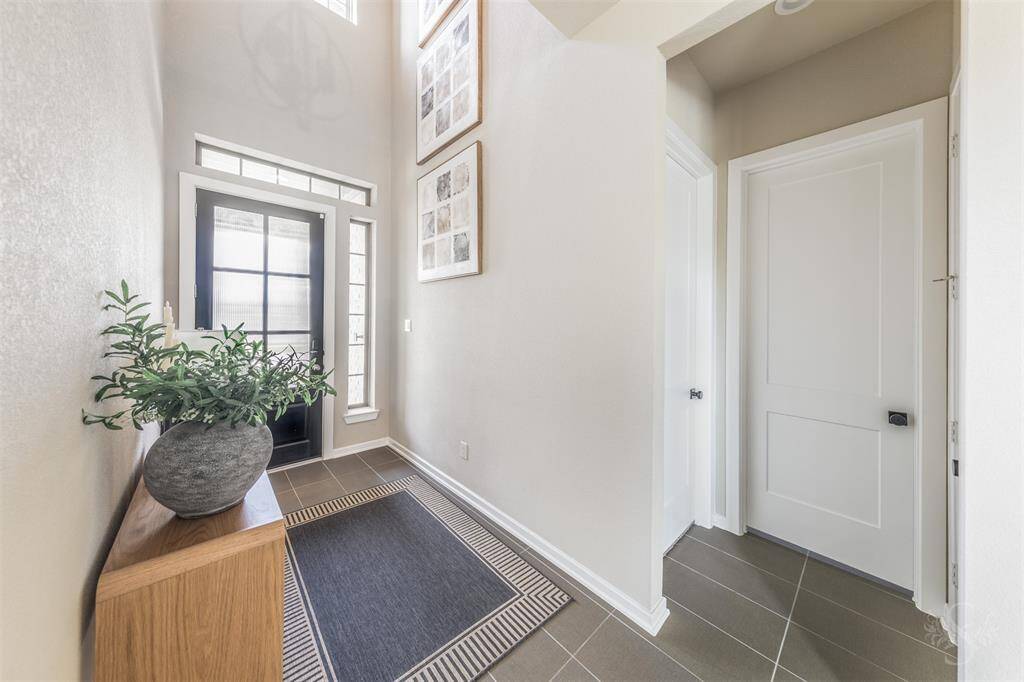 The soaring entryway features sleek tile flooring, a stylish front door with glass panels, and abundant natural light. Clean lines and neutral tones create an inviting and sophisticated first impression.