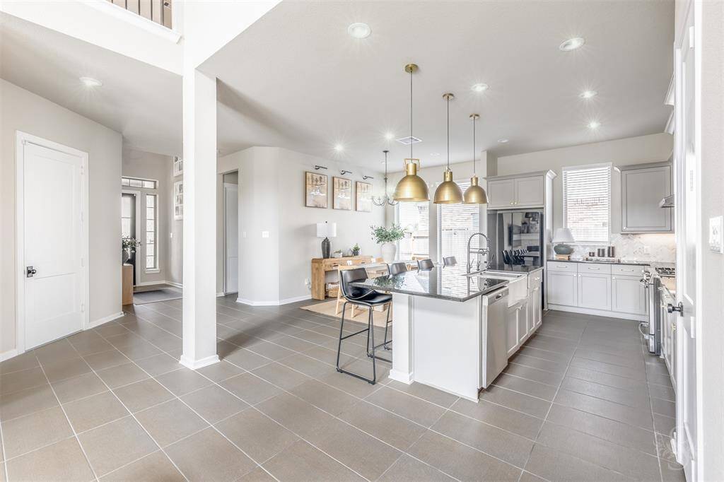 The heart of the home features a stylish kitchen with gray cabinetry, granite countertops, and dramatic pendant lighting over the large island. The open dining area offers an easy flow for everyday living and entertaining.