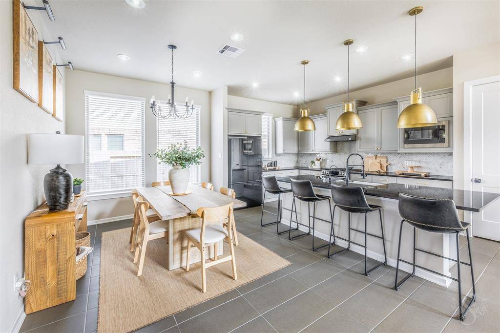 Beautiful open kitchen and dining area featuring a spacious granite island with a breakfast bar, upgraded lighting, and popular gray cabinetry. The seamless flow creates an ideal space for everyday living and entertaining.