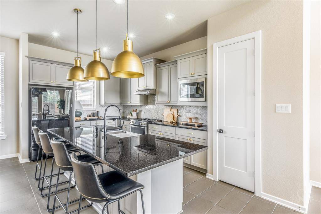 The chef’s kitchen boasts popular gray cabinetry with upgraded handles and knobs, stainless steel appliances, farmhouse sink, a herringbone backsplash, and a granite island with breakfast bar. Elegant gold pendant lighting adds a luxurious touch to this beautiful gathering space.