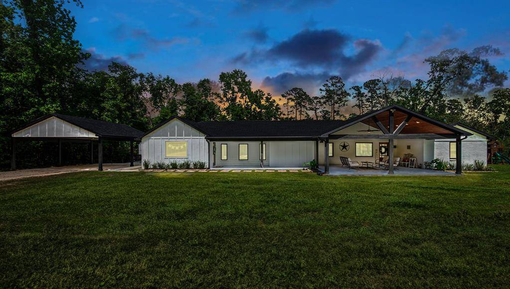 This photo features a charming, single-story home with a modern farmhouse design, nestled amidst lush greenery. It boasts a spacious covered patio, perfect for outdoor relaxation, and a generous lawn area. The setting is serene and inviting, ideal for nature lovers and those seeking tranquility.