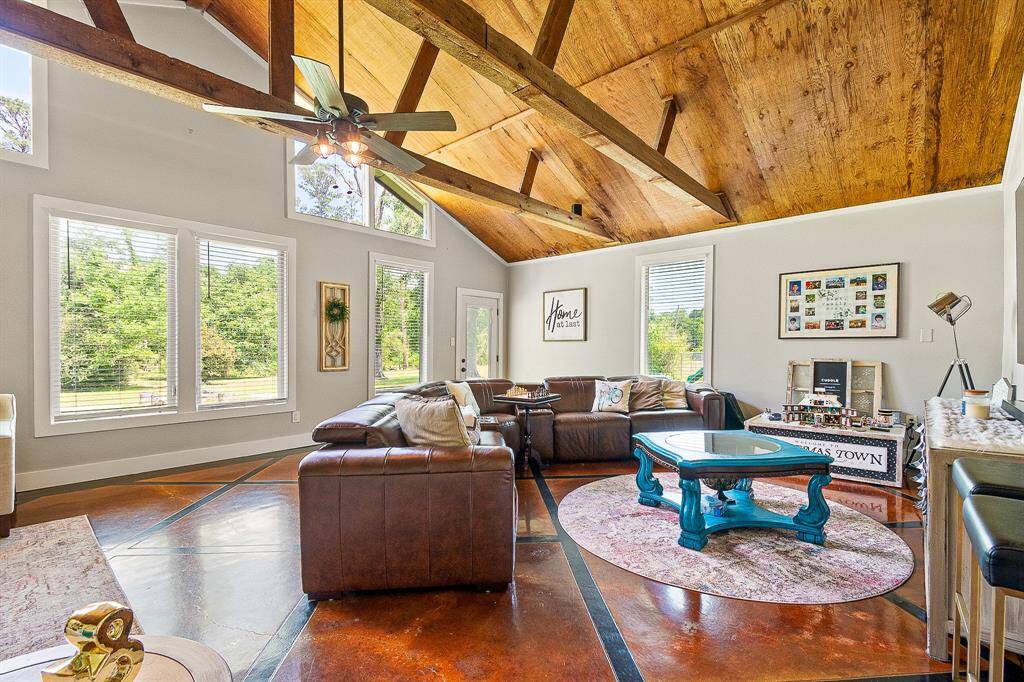 This spacious living room features high vaulted ceilings with exposed wood beams, large windows offering abundant natural light and scenic views and polished concrete floors. It creates a welcoming and stylish environment perfect for relaxation and entertaining.