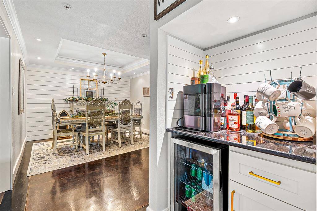 This photo showcases a sophisticated dining room with elegant chandeliers and complemented by a cozy beverage nook featuring a mini-fridge and countertop bar area. The space is inviting, with shiplap walls and a warm, ambient atmosphere perfect for entertaining.