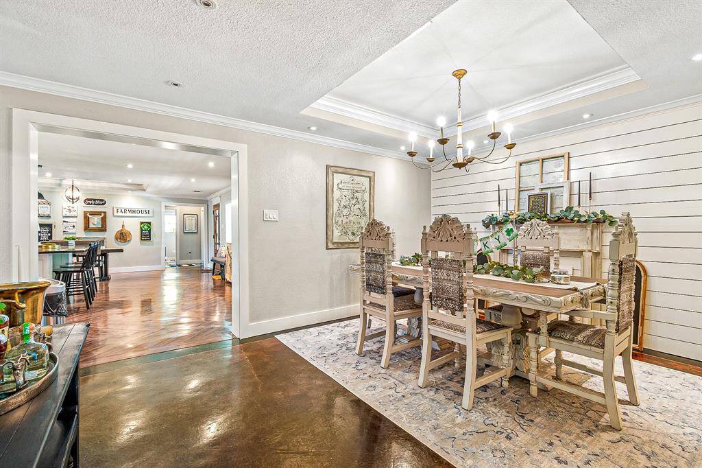 This photo showcases a charming dining area with and an elegant chandelier. The room features a shiplap accent wall and opens into a spacious, well-lit kitchen area with hardwood floors, creating a warm and inviting atmosphere.