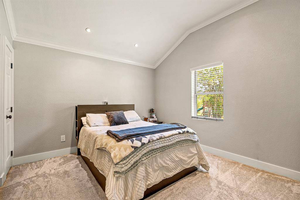 This guest bedroom features a cozy space with neutral walls, recessed lighting, and a large window offering natural light.