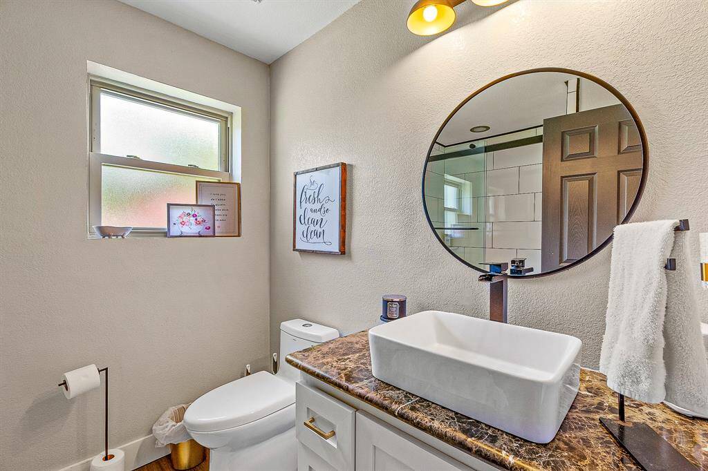 The guest modern bathroom with a sleek design featuring a round mirror, vessel sink, and neutral tones. Ample natural light from a frosted window enhances the clean, inviting atmosphere.