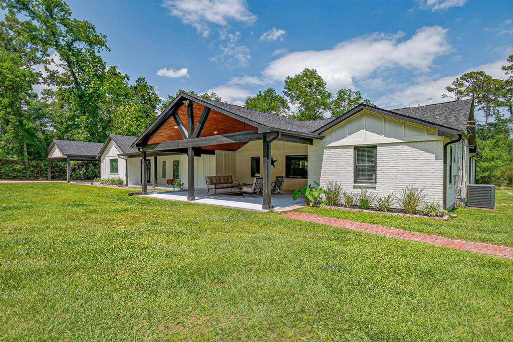 This home features a modern ranch-style design with a spacious covered porch, white brick exterior, and black accents. It is set on a large, grassy lot with mature trees, offering a serene and inviting atmosphere.