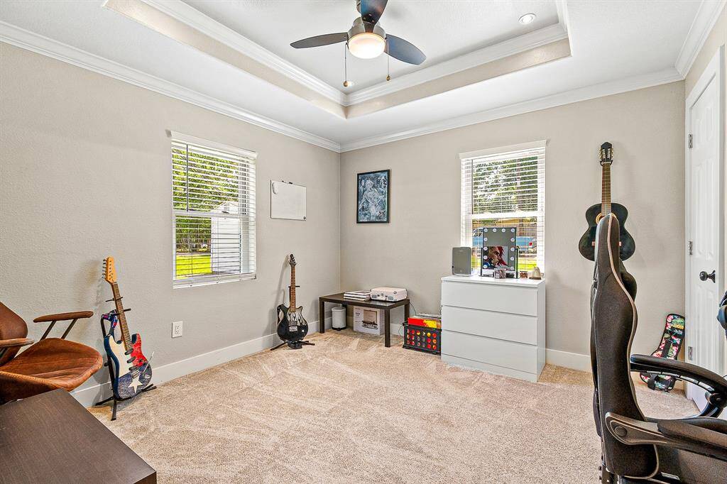 This guest room is a bright with neutral walls, featuring a tray ceiling and a ceiling fan. It has two windows allowing natural light.