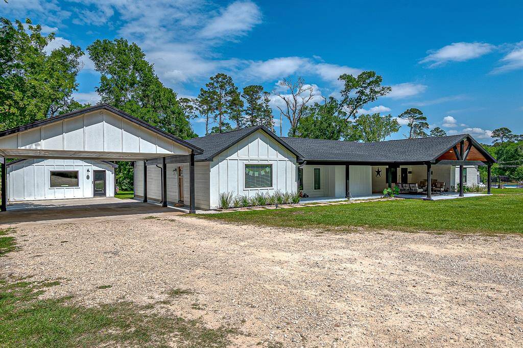 This photo showcases a charming single-story home with a modern farmhouse design. It features a spacious front porch, a carport, and a large yard.