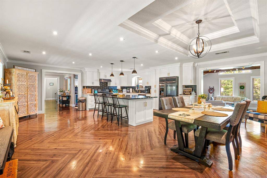 This spacious, open-concept kitchen and dining area features elegant hardwood floors, modern white cabinetry, and a large island with bar seating. Ample natural light and stylish lighting fixtures create a warm, inviting atmosphere, perfect for entertaining.