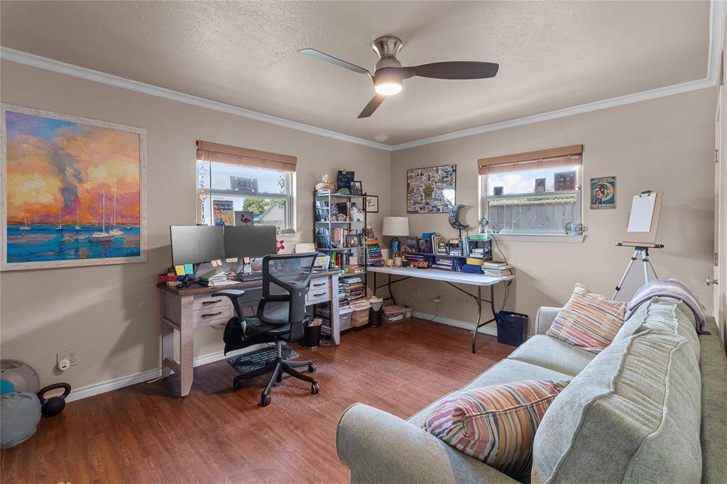 This photo shows a cozy home office (downstairs bedroom) with wooden floors, neutral walls, and a ceiling fan.