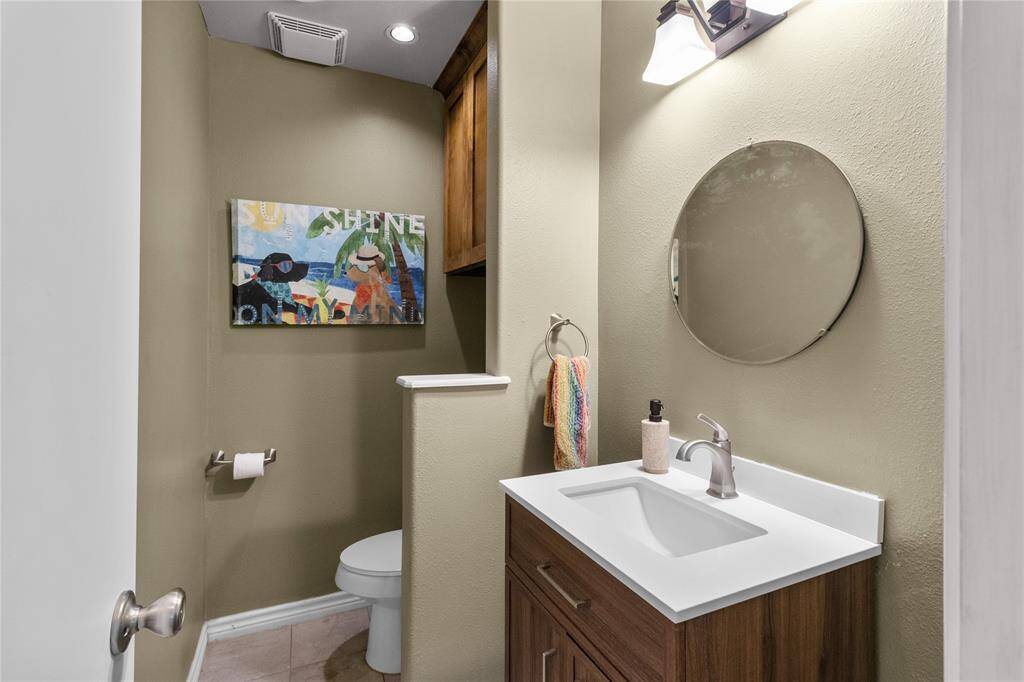 This is a modern half-bathroom featuring a sleek vanity with a white countertop, a round mirror, and warm green walls. It has a new vanity and a wall-mounted light fixture, creating a cozy and inviting atmosphere.