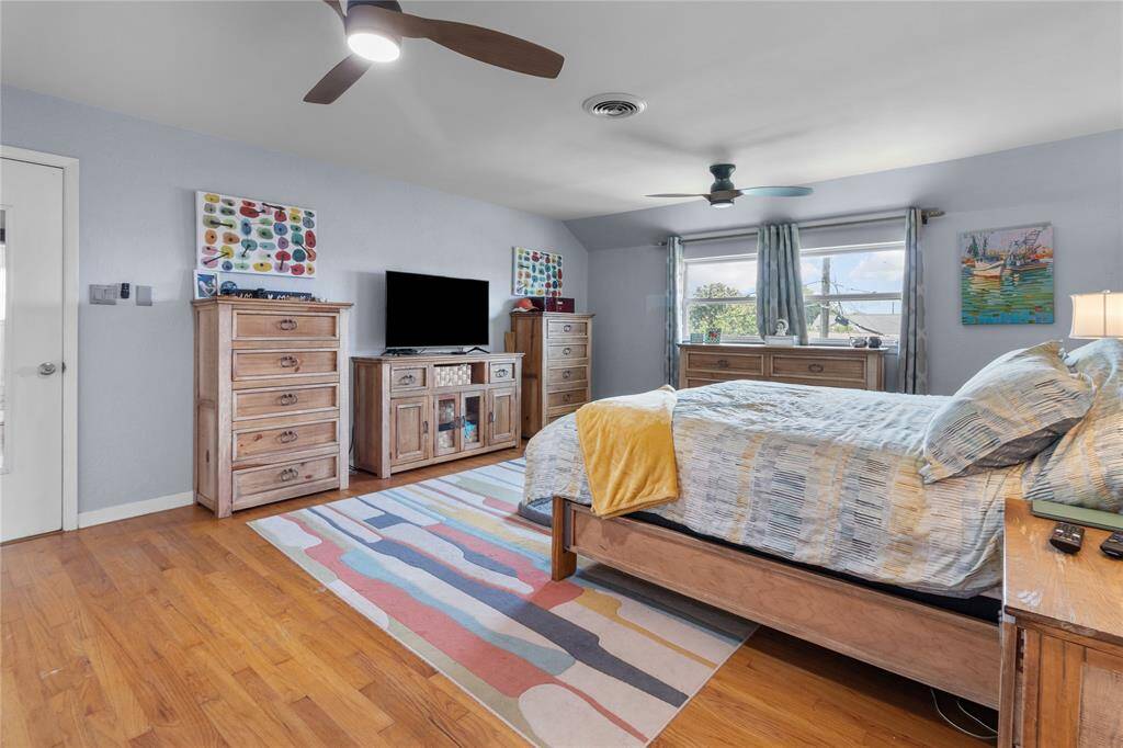 This spacious second story primary bedroom features hardwood floors, modern ceiling fans, and abundant natural light from large windows.