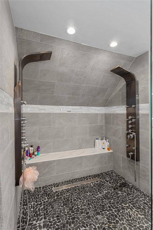 This photo showcases a modern walk-in shower with dual rainfall showerheads, wall jets, and a sleek stone floor. It features a built-in bench and stylish gray tile walls, creating a spa-like atmosphere.