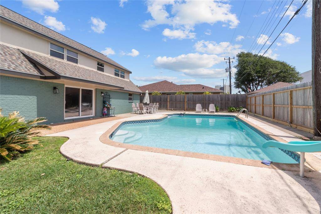 This photo showcases a spacious backyard with a large swimming pool, surrounded by a concrete deck and a privacy fence. The house features a sliding glass door leading to the pool area, perfect for outdoor entertaining.