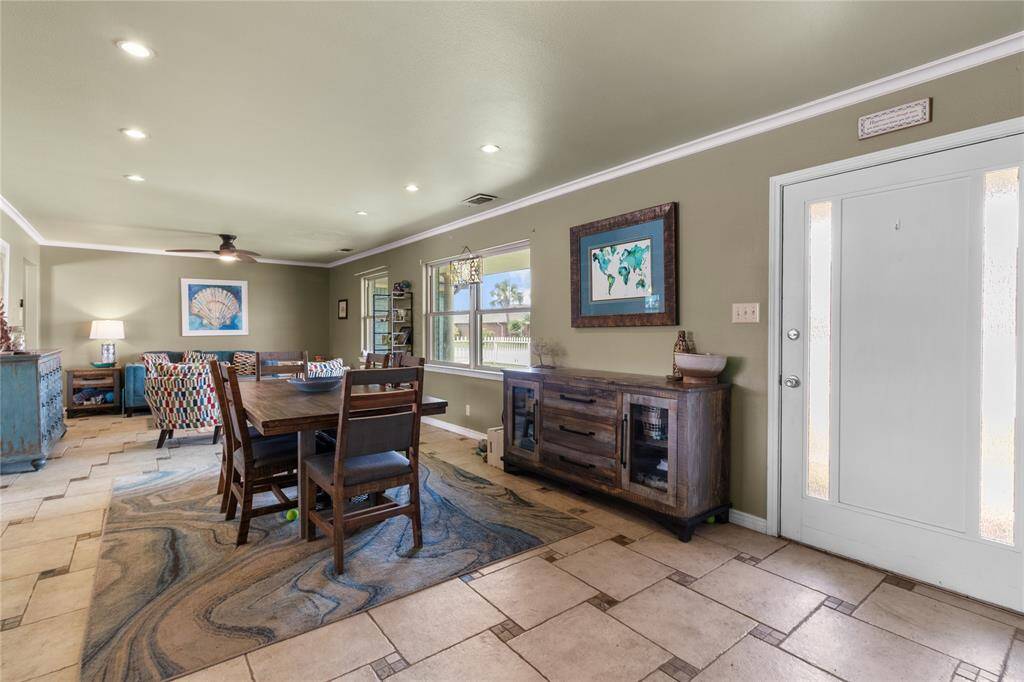 This photo shows a spacious, open-concept living and dining area with stylish tile flooring and green walls. It features a modern ceiling fan, recessed lighting, and large windows for natural light.